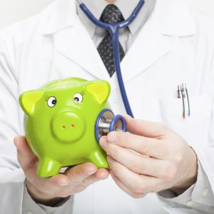 Medical doctor holding stethoscope and piggybank in hand - studio shot