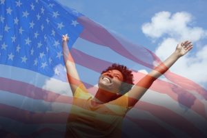 Portrait of cheerful young woman standing outside with her hands raised towards sky
