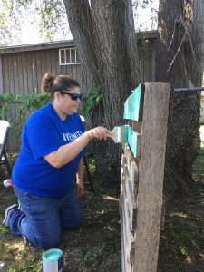 Melissa Guy knees while painting a pallet seafoam green.